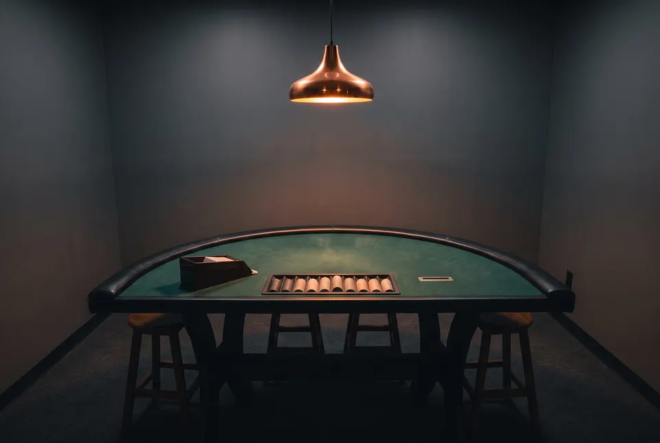 Generated scene: an empty semicircular blackjack table with green felt, a card shoe and a chip tray under a copper pendant lamp in a dark room.